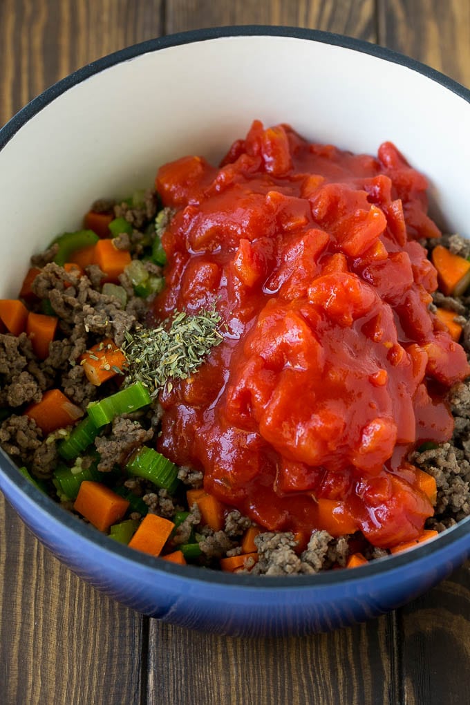 Ground beef, vegetables, canned tomatoes and seasonings in a pot.