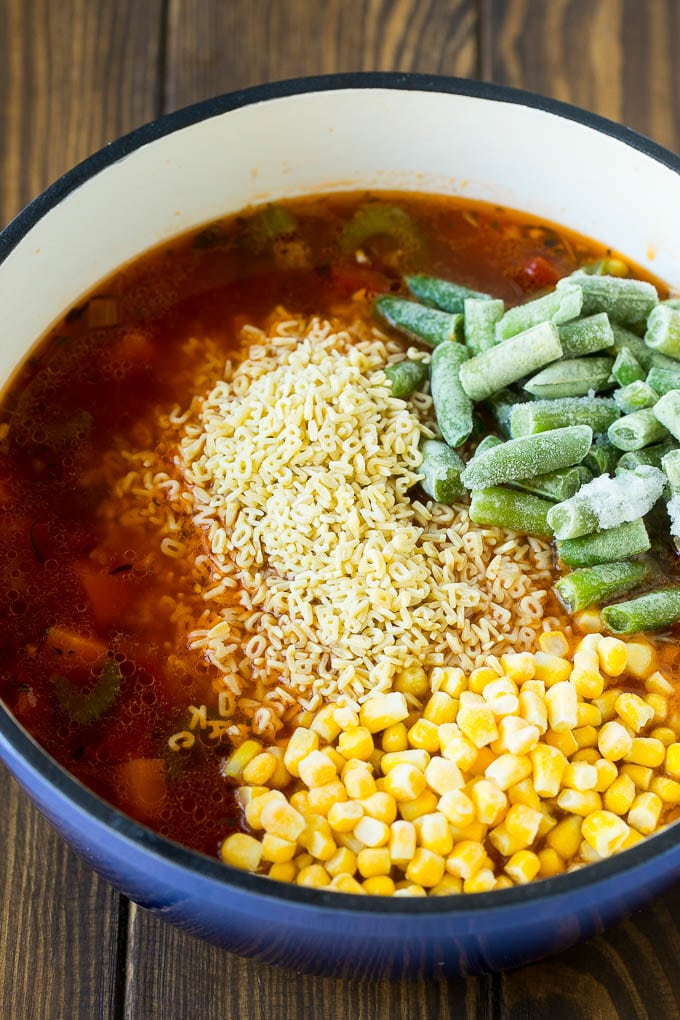 A pot with noodles, broth, frozen corn and frozen green beans.