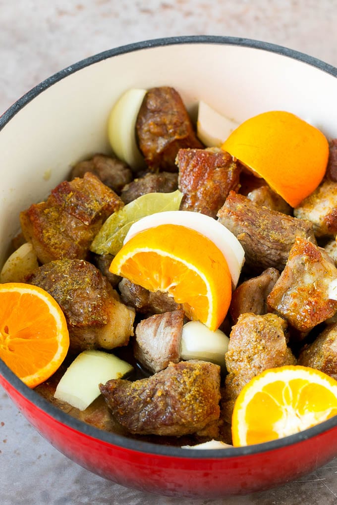 Pork shoulder pieces, oranges and onion in a pot.