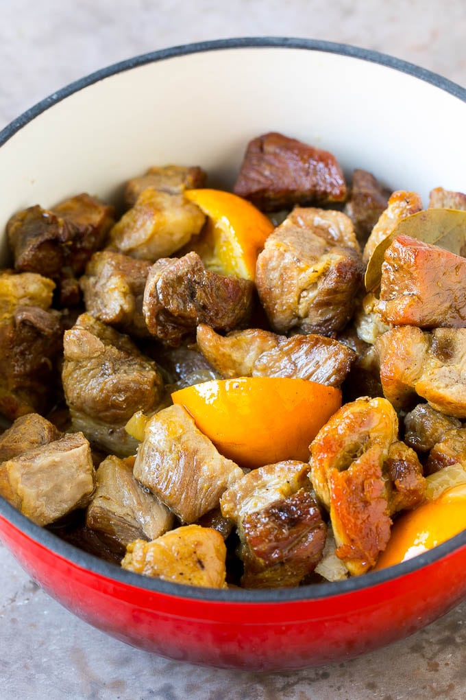 Cooked pork carnitas in a red pot with oranges.