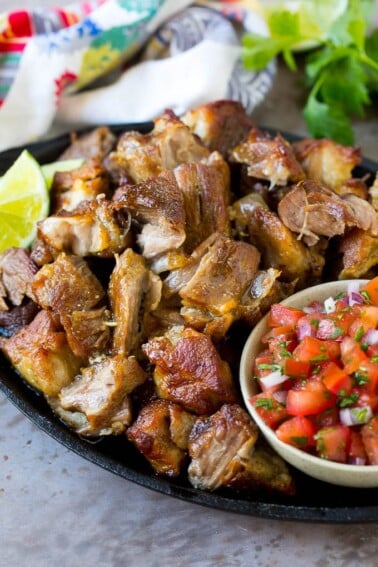 A skillet of pork carnitas served with fresh salsa.