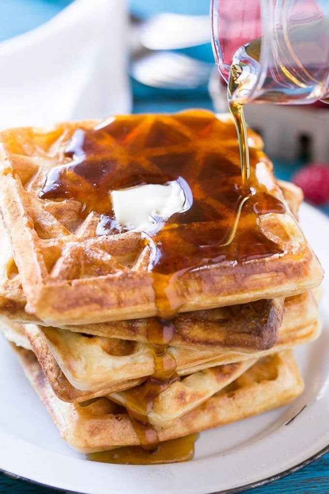 A stack of yeast waffles topped with butter and maple syrup.