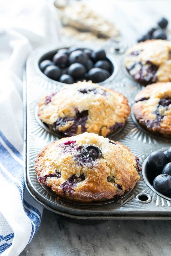 Healthy blueberry muffins in a muffin tin with fresh blueberries as garnish.