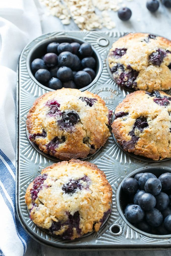 An overhead view of muffins in a tin with fresh blueberries.