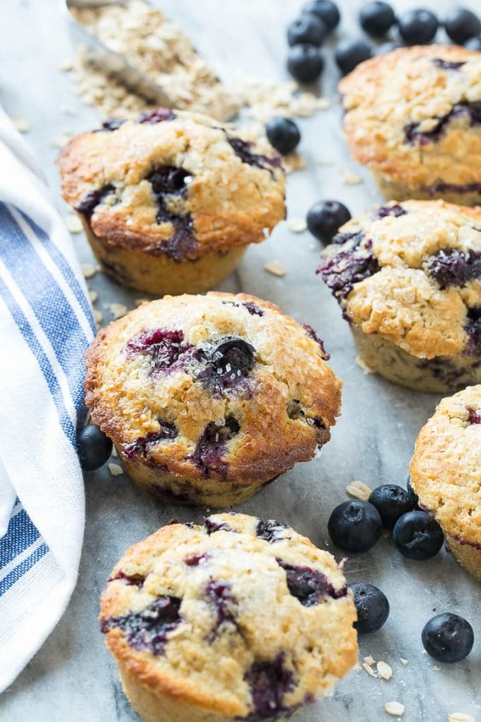 Multiple healthy blueberry muffins on a marble slab with fresh blueberries.