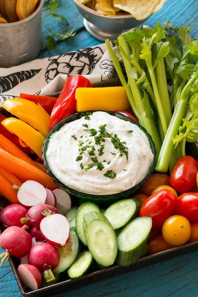 A bowl of homemade ranch dip surrounded by fresh vegetables.