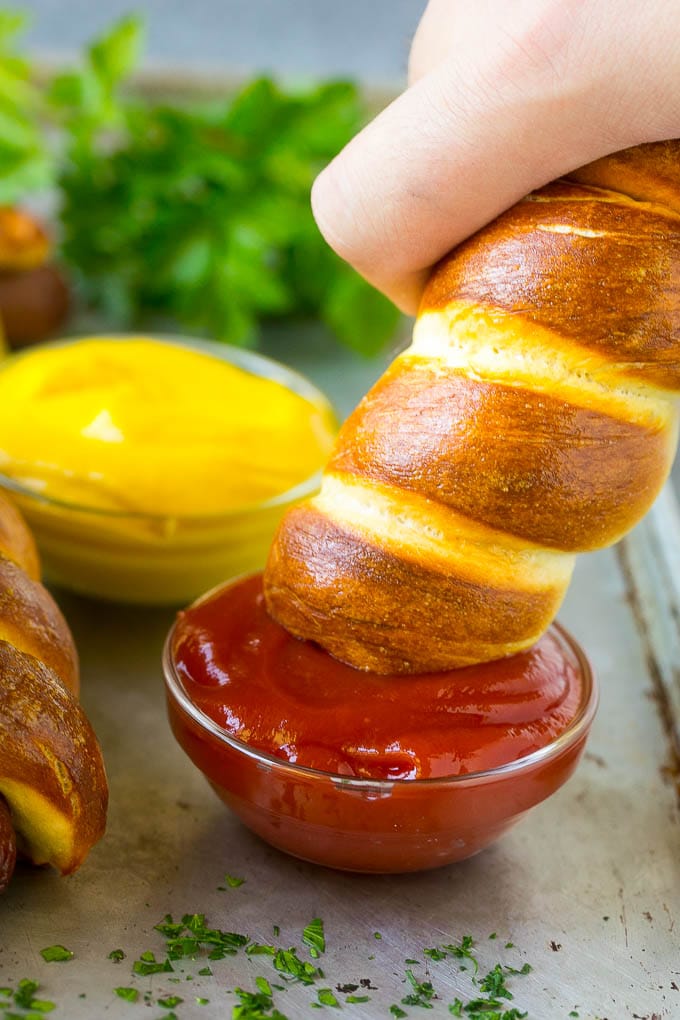 A bagel dog being dipped into a bowl of ketchup.