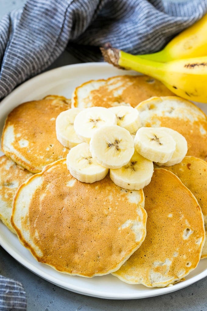 A plate of banana pancakes topped with fresh bananas.