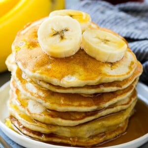 A stack of banana pancakes with banana slices and maple syrup.