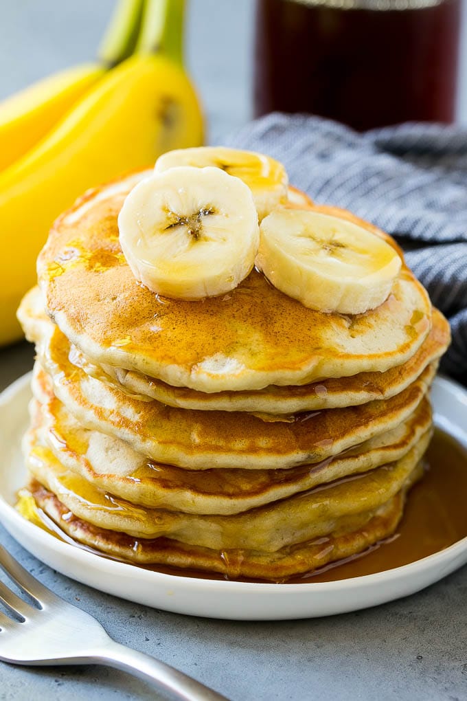 A stack of banana pancakes with banana slices and maple syrup.