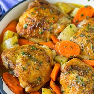 Braised chicken thighs with carrots and potatoes in a skillet.