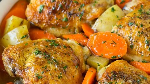 Braised chicken thighs with carrots and potatoes in a skillet.