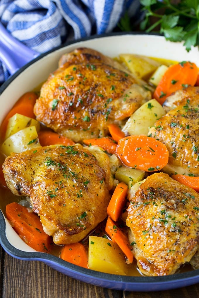 Braised chicken thighs with carrots and potatoes in a skillet.