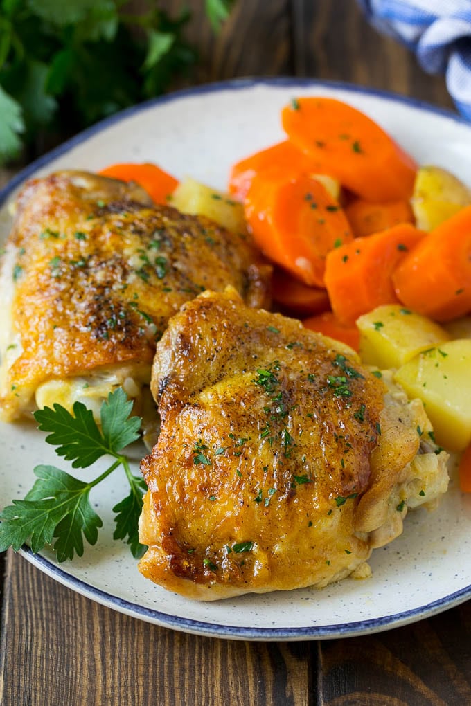 A plate with braised chicken, carrots, potatoes and parsley.