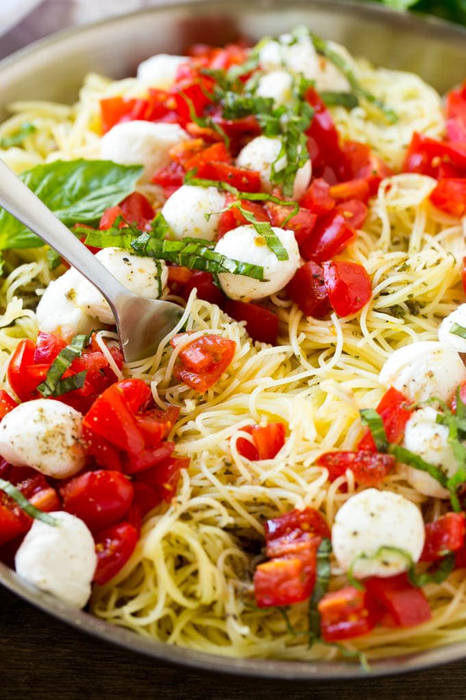 A pan of caprese pasta with angel hair pasta, olive oil, fresh basil, tomatoes and mozzarella cheese.