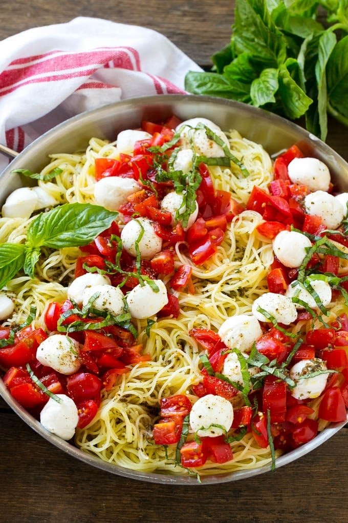 A pan of angel hair caprese pasta topped with olive oil, tomatoes, basil and fresh mozzarella.