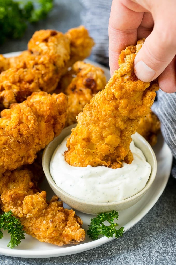A chicken finger being dipped into ranch sauce.