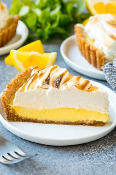 A slice of lemon meringue tart with creamy lemon filling and brown sugar meringue topping.