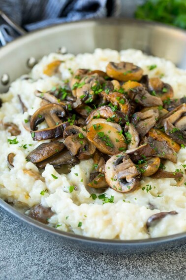 A skillet of mushroom risotto topped with seared mushrooms and parsley.