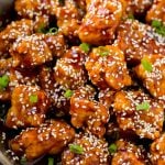 Crispy sesame chicken in a pan, coated in a sweet and savory sauce and sesame seeds.