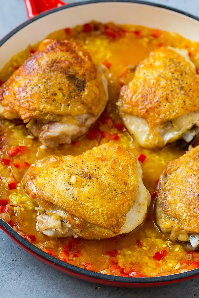 Muslos de pollo, arroz, caldo de pollo y verduras en una sartén.