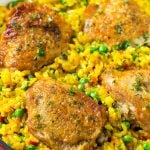 A pan of arroz con pollo with chicken thighs, saffron rice and peas.