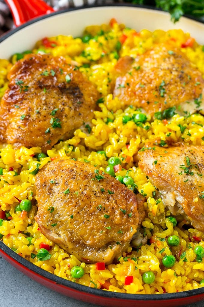 A pan of arroz con pollo with chicken thighs, saffron rice and peas.
