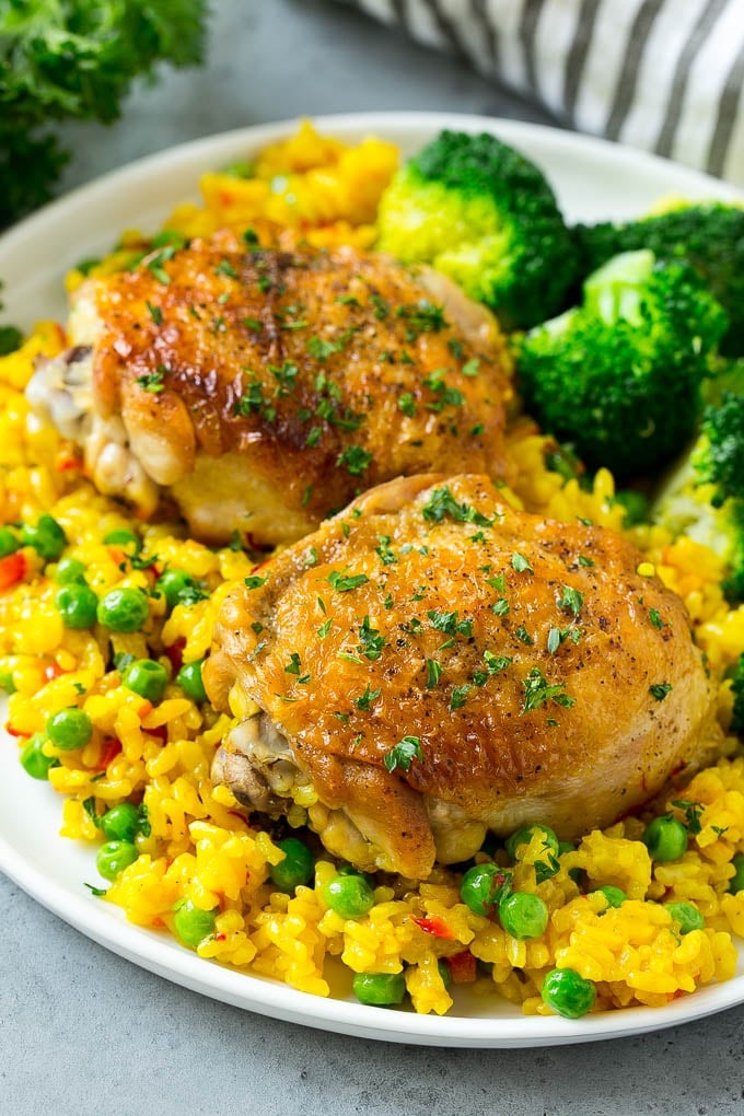 A plate of Spanish Arroz con Pollo with chicken thighs, rice and a side of broccoli.