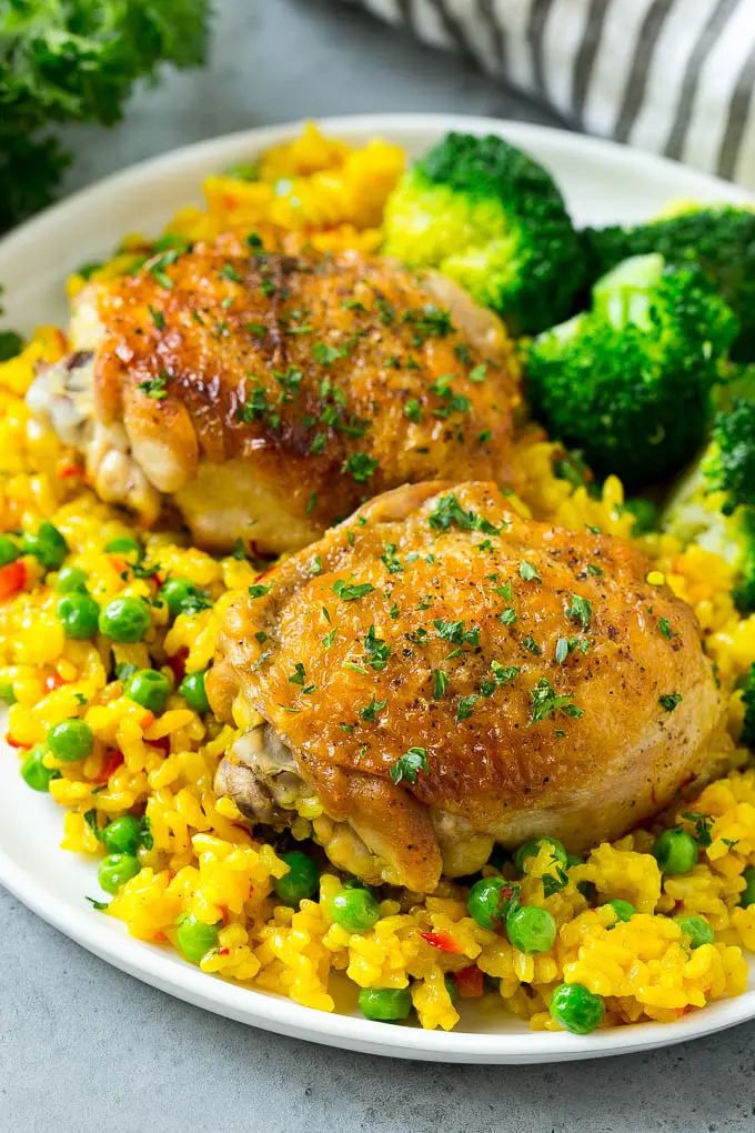 Un plato de Arroz con Pollo español con muslos de pollo, arroz y una guarnición de brócoli.