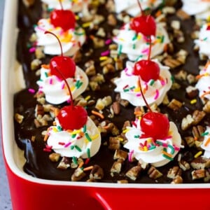 Banana split cake topped with hot fudge, whipped cream, sprinkles and cherries.