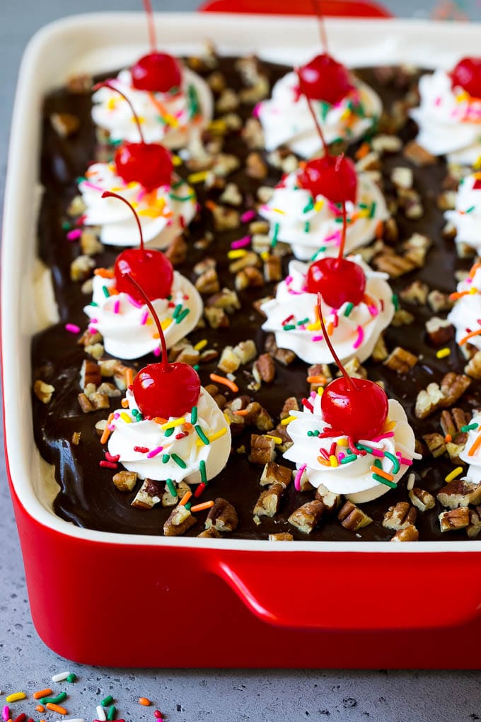 Banana split cake topped with hot fudge, whipped cream, sprinkles and cherries.