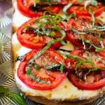 A split loaf of bread on a sheet pan topped with fresh mozzarella cheese, sliced red tomatoes, thinly sliced basil and balsamic glaze.