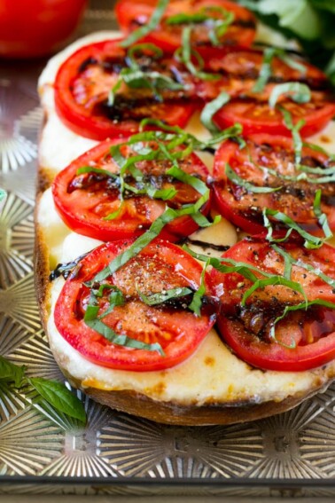 A split loaf of bread on a sheet pan topped with fresh mozzarella cheese, sliced red tomatoes, thinly sliced basil and balsamic glaze.