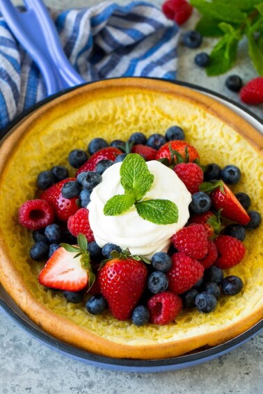 A Dutch baby puffed pancake in a skillet, topped with berries and whipped cream.