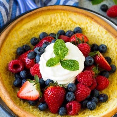 A Dutch baby puffed pancake in a skillet, topped with berries and whipped cream.