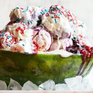 This recipe for a Red White and Blueberry Sundae is a watermelon loaded with three types of ice cream, homemade strawberry and blueberry sauces, marshmallow topping and the whole thing is finished off with whipped cream, sprinkles and chocolate covered strawberries. It's the perfect show stopper for the 4th of July!