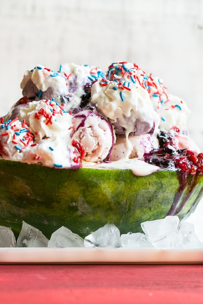 This recipe for a Red White and Blueberry Sundae is a watermelon loaded with three types of ice cream, homemade strawberry and blueberry sauces, marshmallow topping and the whole thing is finished off with whipped cream, sprinkles and chocolate covered strawberries. It's the perfect show stopper for the 4th of July!