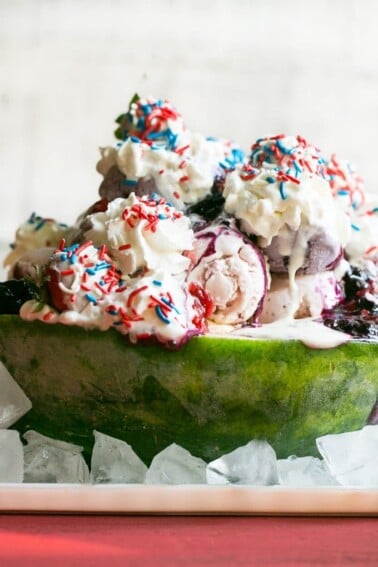 This recipe for a Red White and Blueberry Sundae is a watermelon loaded with three types of ice cream, homemade strawberry and blueberry sauces, marshmallow topping and the whole thing is finished off with whipped cream, sprinkles and chocolate covered strawberries. It's the perfect show stopper for the 4th of July!