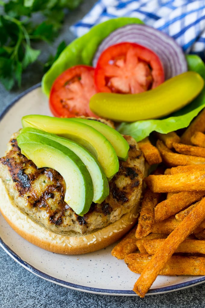 An open faced turkey burger topped with sliced avocado.