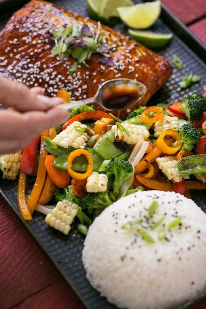 A spoonful of sauce being poured over mixed vegetables.