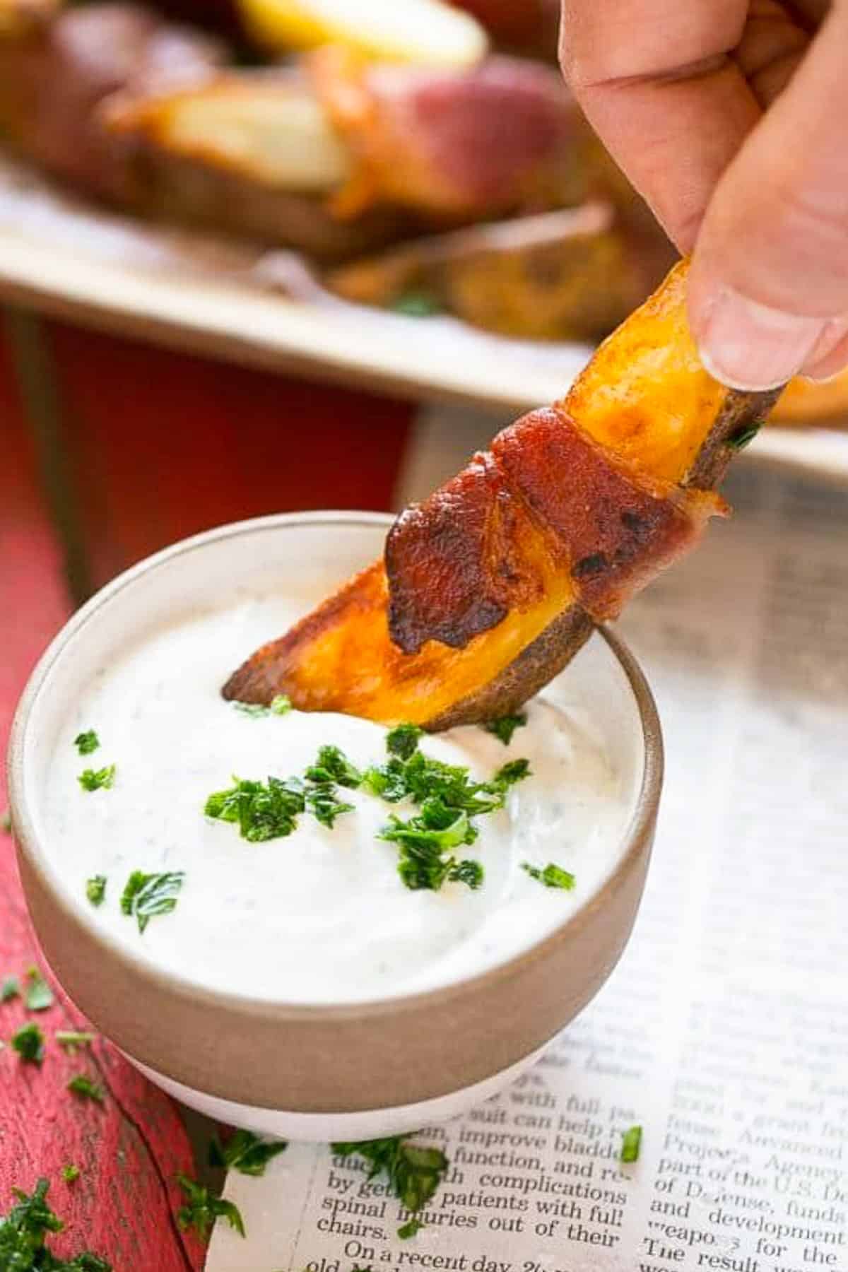 A hand putting bacon wrapped potatoes into ranch dip.
