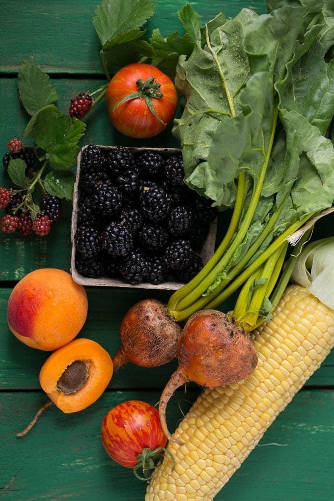 A selection of produce including corn, beets, apricots, tomatoes and blackberries.