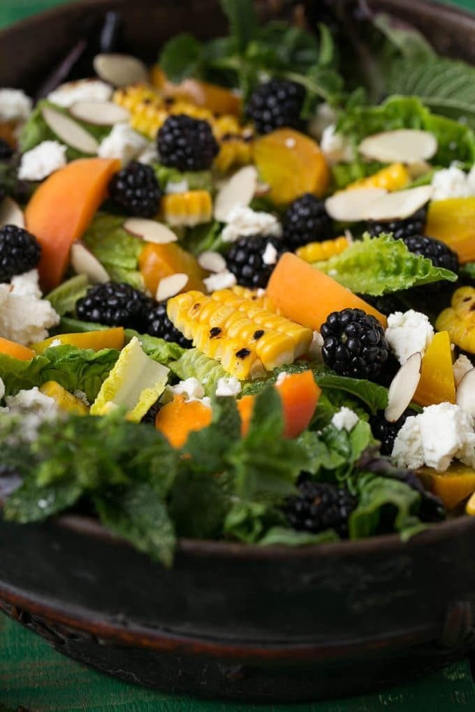 A bowl of lettuce topped with berries, corn, feta cheese and apricots.