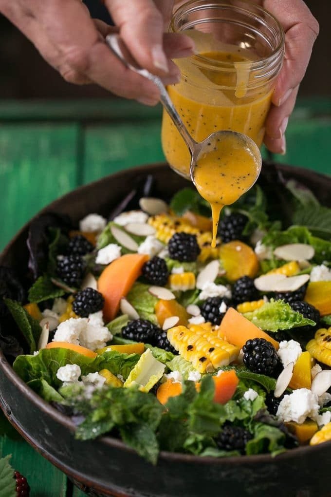 A hand spooning apricot dressing on top of a salad.