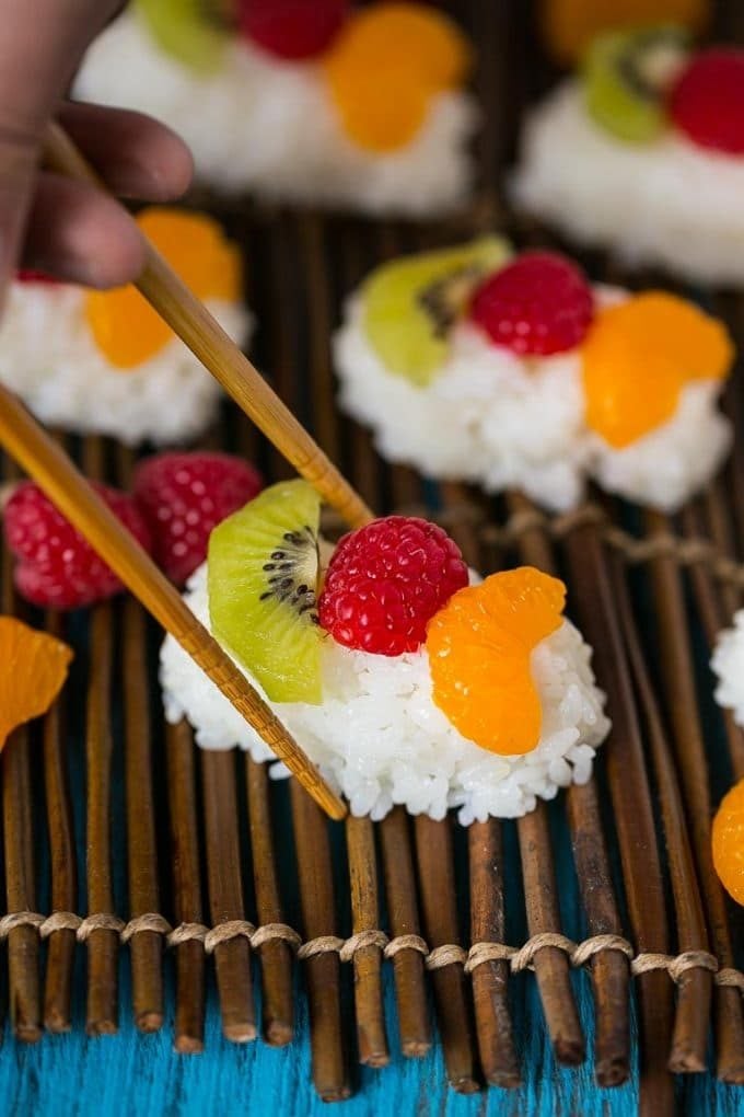 Chopsticks picking up a piece of fruit sushi.