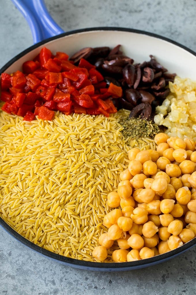 Orzo pasta, olives, chickpeas and roasted peppers in a skillet.