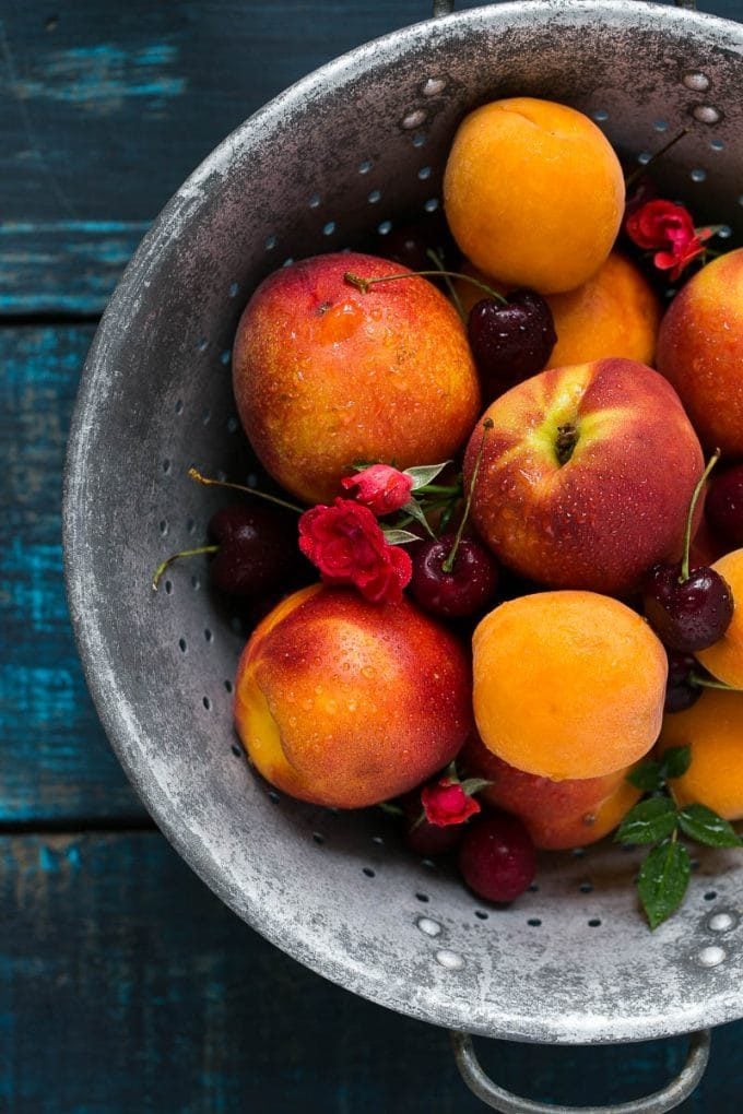 A colander filled with peaches, apricots and cherries.