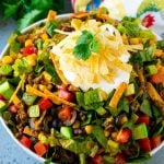 Taco salad made with ground beef, romaine lettuce and vegetables, topped with sour cream and tortilla strips.