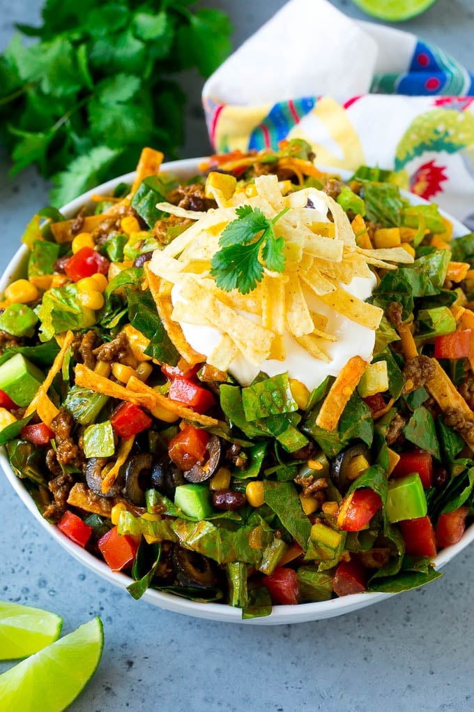 Taco salad made with ground beef, romaine lettuce and vegetables, topped with sour cream and tortilla strips.