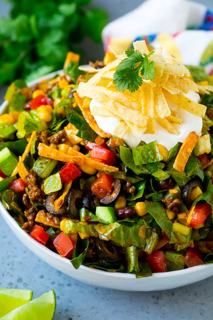 A bowl of taco salad with ground beef, lettuce, tomatoes, cheese and olives.